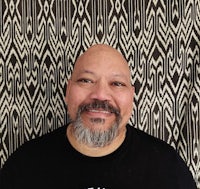 a man with a beard smiling in front of a patterned wall